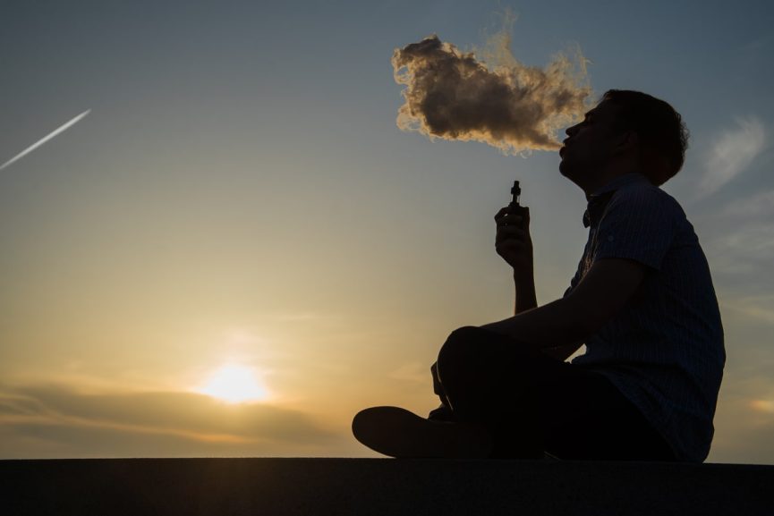 vaping young man produces vapor on sunset sky